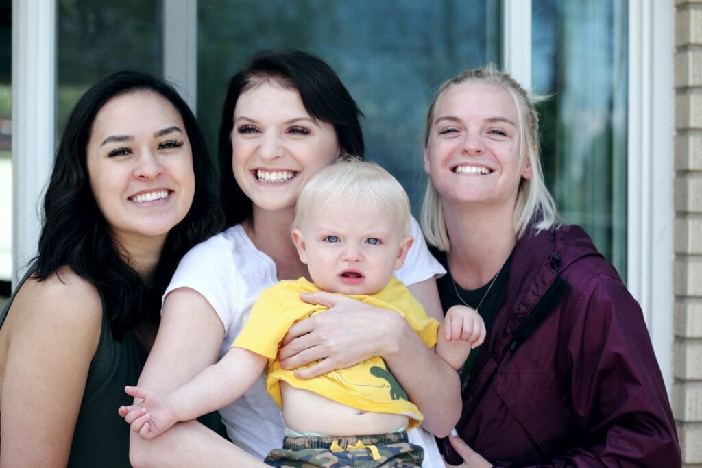 Three smiling women with blond toddler in yellow shirt second parent adoption